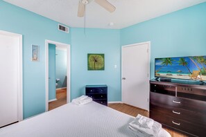 Ein Schlafzimmer mit Bett, Kommode und Fernseher, der eine Strandansicht zeigt.