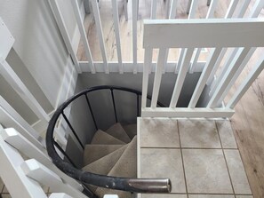 Una escalera de caracol con barandilla blanca que da a un suelo de baldosas.