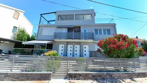 Un immeuble résidentiel moderne à deux étages, doté d’un balcon, d’une entrée sécurisée et d’un mur en pierre.