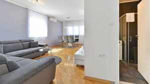 Un salon moderne avec un canapé gris, un coin repas comprenant une table et des chaises, et une douche séparée par des parois en verre.