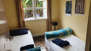 A room with two beds, a window with curtains, a black stool, and two wall-mounted pictures.