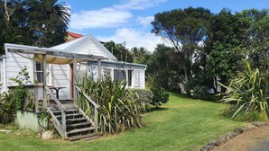 A small, single-story house with a porch, surrounded by lush greenery and a clear sky.