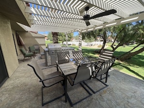 Un patio exterior con una parrilla, asientos y un ventilador de techo.