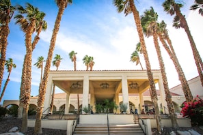 A building with a covered entrance, palm trees, and a clear sky.