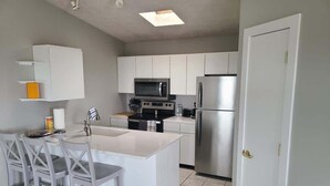 A modern kitchen with white cabinets, a central island with seating, a microwave, stove, and refrigerator. - Bayview Condo #4, Ogallala Beach (Ogallala)
