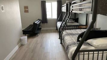 A dormitory room with bunk beds, a desk, and a window with curtains.