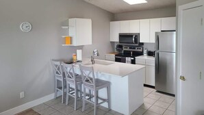 A modern kitchen with white cabinetry, a central island with bar stools, a microwave, stove, and refrigerator. - Bayview Combo Condos 3 & 4, Ogallala Beach (Ogallala)