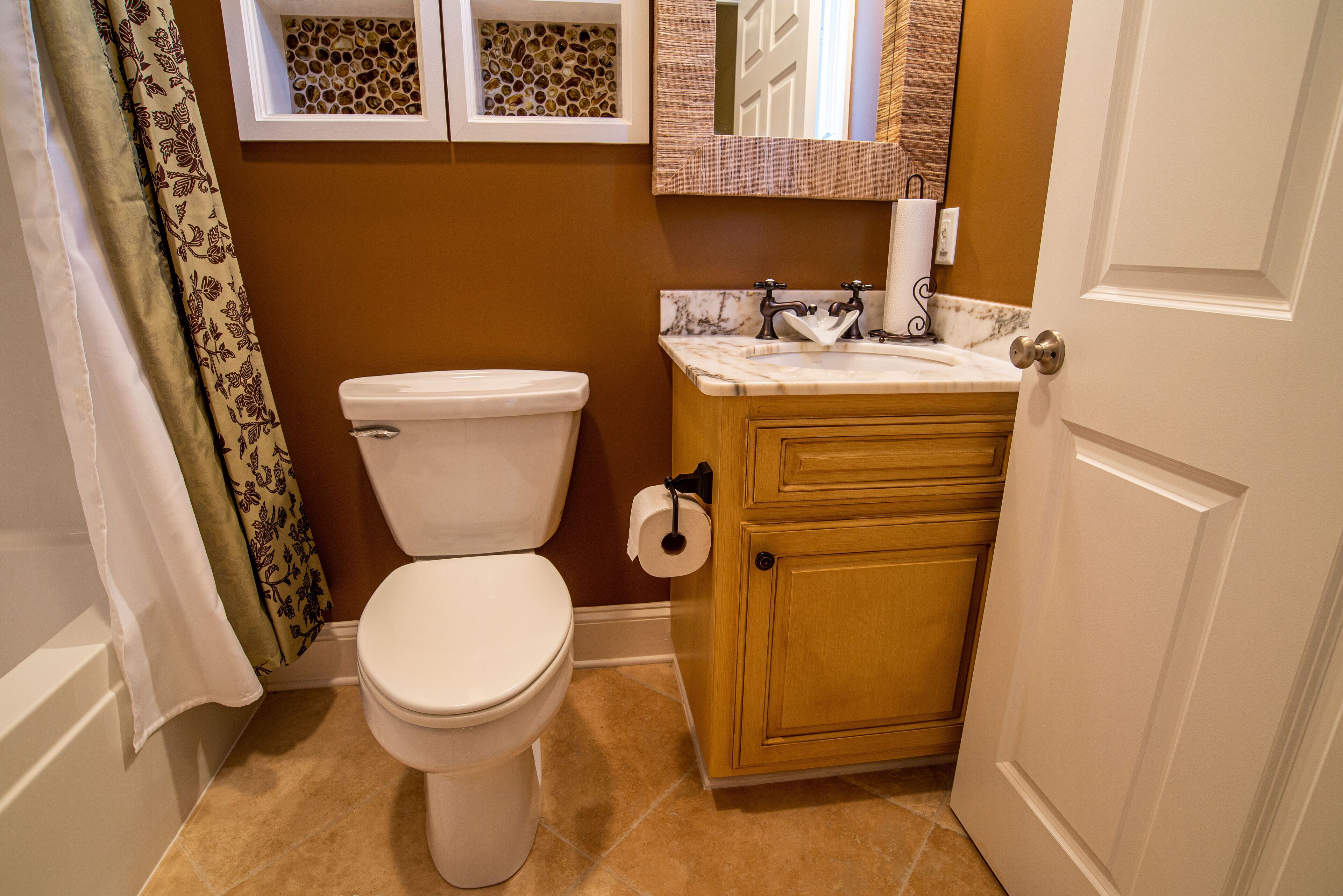Une salle de bain comprenant des toilettes, un meuble en bois, un comptoir en marbre et un miroir fixé au mur.