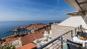Un balcón con mesa lista para comer, con vista a un pueblo costero de edificios históricos y un cielo azul despejado.