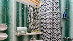 Un baño con azulejos verdes, un lavamanos blanco, un inodoro, una ducha con cortina a rayas y un estante con artículos de tocador.