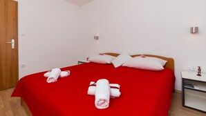 Habitación de hotel con una colcha roja, almohadas blancas y toallas dobladas con cuidado sobre la cama.