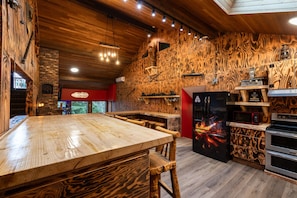 A rustic kitchen with a wooden table, bar stools, a refrigerator with a decorative design, and a brick wall. - AirD&D !!! (Chilliwack)
