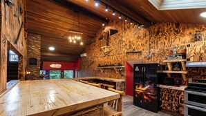 A rustic kitchen with a wooden table, a brick oven, and a black refrigerator with a lava design.