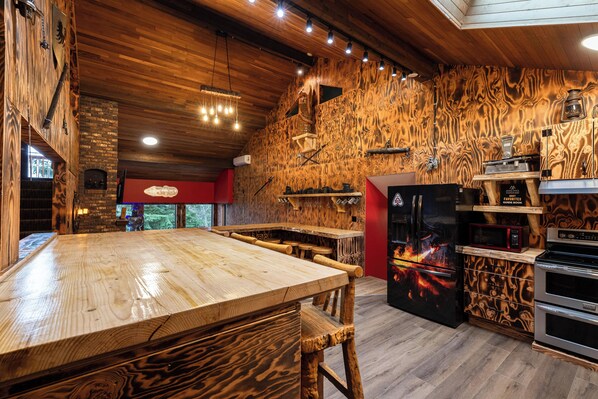 A rustic kitchen with a wooden table, a brick oven, and a black refrigerator with a lava design.