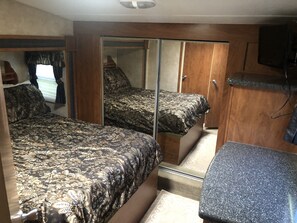 A compact RV bedroom with two beds, a mirrored closet, and a small kitchenette. - River access! Clean & comfy 5th wheel, located near the famous Kenai River (Soldotna)