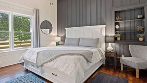 Een slaapkamer met een groot bed, een nachtkastje, een stoel, een spiegel en een plank met planten.