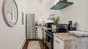 Een moderne keuken met roestvrijstalen apparatuur, een granieten aanrechtblad en een decoratieve wandkunst met een boom.