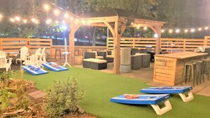 Een terras buiten met zitplaatsen, een houten pergola en lichtjes.