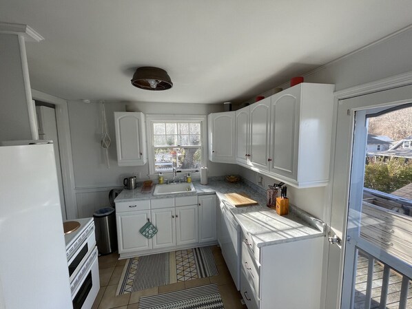Compact kitchen with oven, sink, and window offering a neighborhood view.
