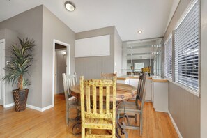 Un comedor con una mesa y sillas de madera, una planta en maceta y una cocina al fondo.