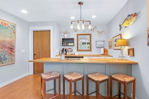 A kitchen with a central island, bar stools, a chandelier, and wall-mounted decorations.