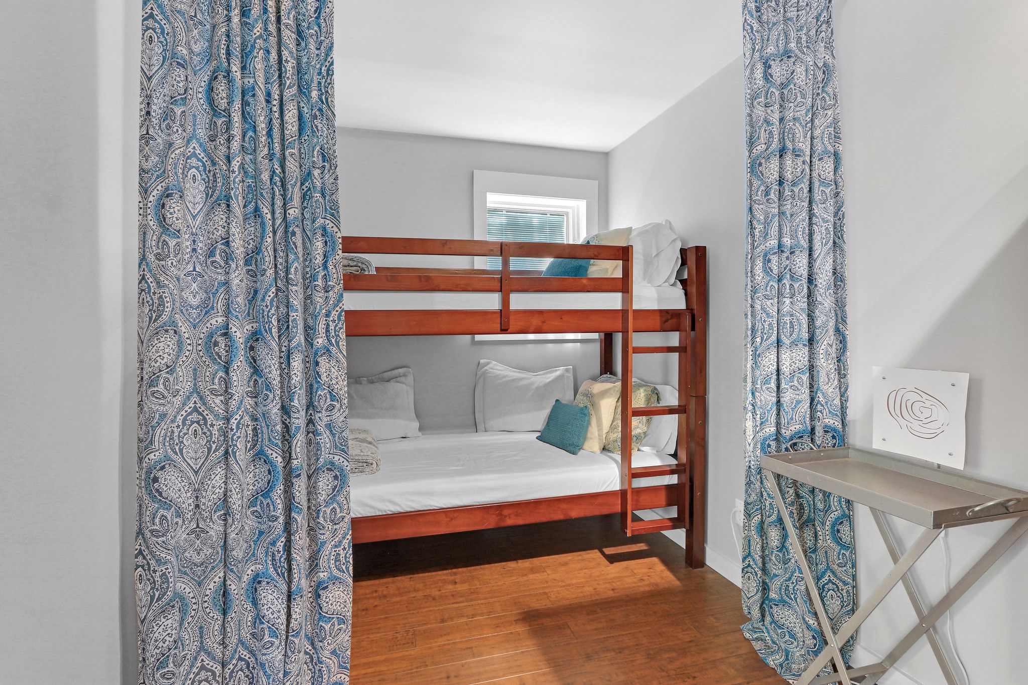 A bunk bed with a wooden frame, a bedside table, and a window with blinds.