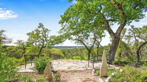 Un patio de piedra con dos bancos, rodeado de follaje y árboles.