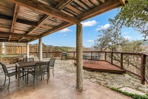 Un patio al aire libre con mesa y sillas de madera, suelo de piedra y vistas del paisaje circundante.