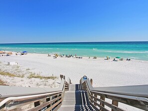 A beach with a wooden staircase leading down to the sand, a clear blue sky, and a calm sea.