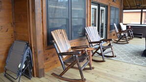 A wooden cabin with rocking chairs and a folding chair near the entrance. - Riverfront cabin on the Toccoa River w/hot tub  NO HIDDEN FEES (Mineral Bluff)