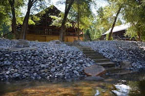 A wooden cabin with a stone staircase leading to a wooden deck, surrounded by trees and a small stream. - Riverfront cabin on the Toccoa River w/hot tub NO HIDDEN FEES (Mineral Bluff)