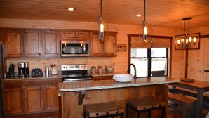 A wooden cabin-style kitchen with a central island, stainless steel appliances, and a large window. - Riverfront cabin on the Toccoa River w/hot tub  NO HIDDEN FEES (Mineral Bluff)