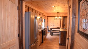 A wooden interior with a kitchen area featuring a refrigerator, a dining table, and a bench. - Riverfront cabin on the Toccoa River w/hot tub  NO HIDDEN FEES (Mineral Bluff)