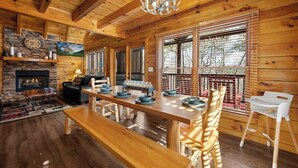 A wooden cabin interior with a fireplace, dining table, and large windows. - Pigeon Forge|Pool·Hot Tub|Game&Theater Rm·Pets·EV (Pigeon Forge)