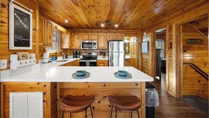 A wooden cabin-style kitchen with a central island, white countertops, and wooden cabinets. - Pigeon Forge|Pool·Hot Tub|Game&Theater Rm·Pets·EV (Pigeon Forge)