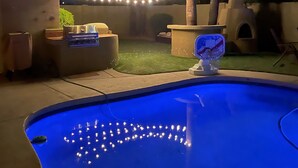 Un espace extérieur avec piscine, agrémenté de guirlandes lumineuses, d’un jacuzzi et d’un élément décoratif aquatique.