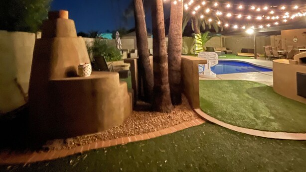 Un jardin avec une piscine, des palmiers et des guirlandes lumineuses.