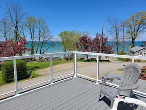 A deck with a view of a beach and ocean, a chair, and a table. - Spectacular Lake Erie Sunsets with beach access (North East)