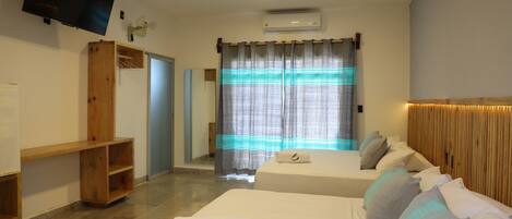 Habitación de hotel con dos camas, televisión de pantalla plana, aire acondicionado y un estante de madera.