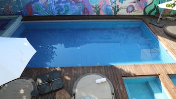 Una piscina con bordo in legno, lettini e un murale colorato.