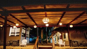 A covered outdoor seating area with wooden chairs and a thatched roof.
