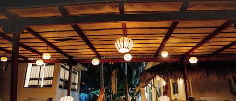 A covered outdoor seating area with wooden chairs and a thatched roof.