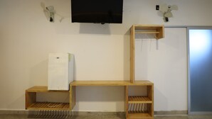 A room with a flat-screen TV mounted on the wall, a wooden shelf unit, and a refrigerator.