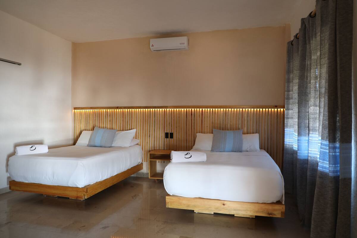 A hotel room with two beds, a wooden headboard, and a ceiling-mounted air conditioner.