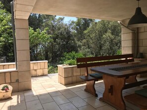 Relax on the sheltered patio with a wooden bench and table, surrounded by lush greenery and a structured design.