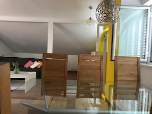 Relax in this stylish living room with a glass dining table, comfortable sofa, and high ceiling with exposed beams.