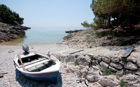 Moored on a rocky beach, this single-person boat offers a serene view of the calm sea and distant shoreline.