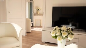 Ein modernes Wohnzimmer mit einem weißen Sofa, einem weißen Couchtisch, einem Flachbildfernseher und einer Vase mit weißen Blumen.