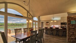 Uma ampla área de refeições com vista para um lago, uma cozinha com detalhes em pedra e um espaço de bar com banquetas.