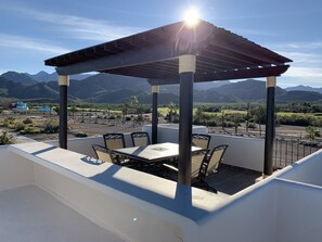 An outdoor patio with a pergola, a table, and chairs, overlooking a mountainous landscape.